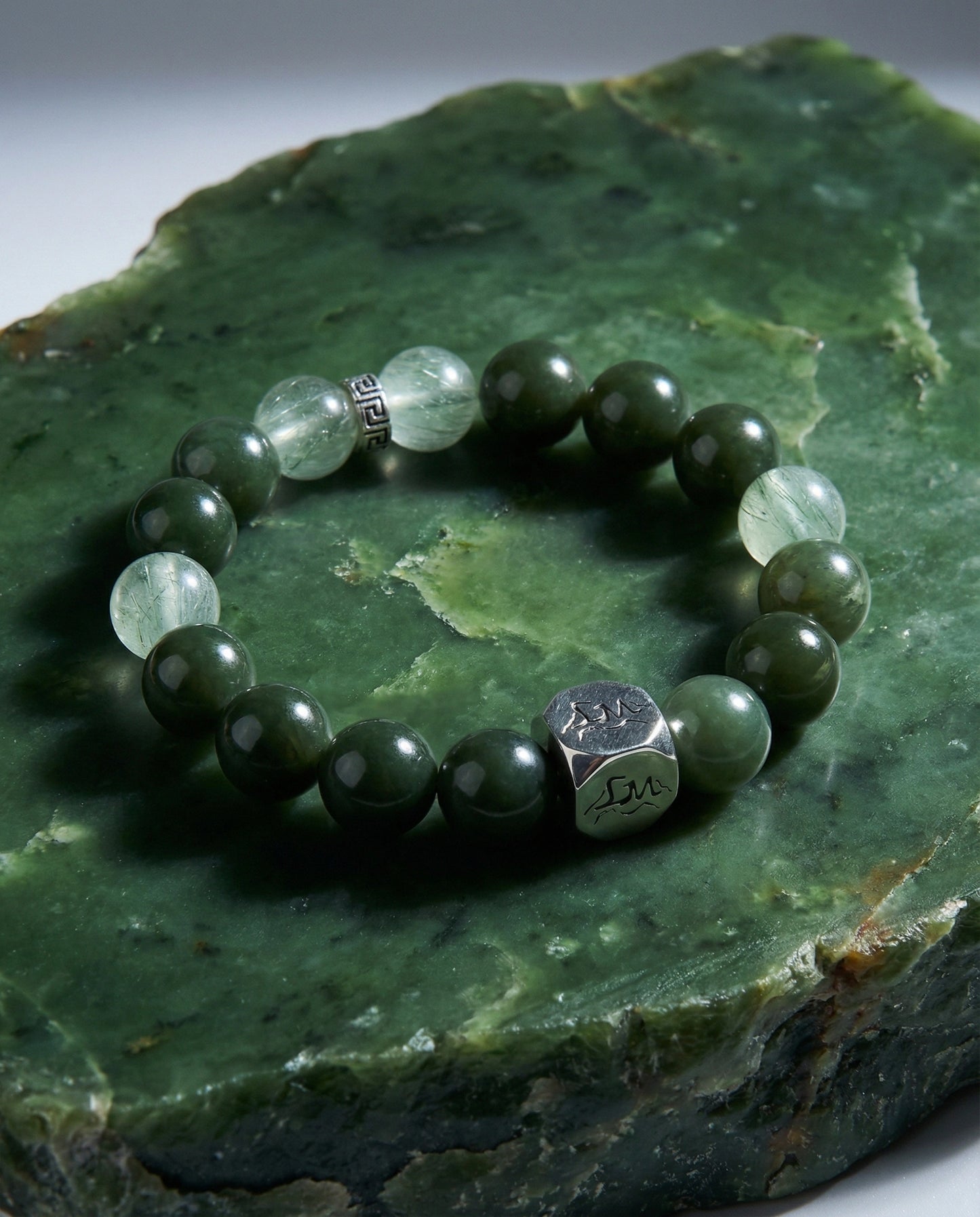 Aegis wood crystal bracelet — nephrite jade and green rutilated quartz — on raw nephrite jade mineral slab — Leymen Jewels