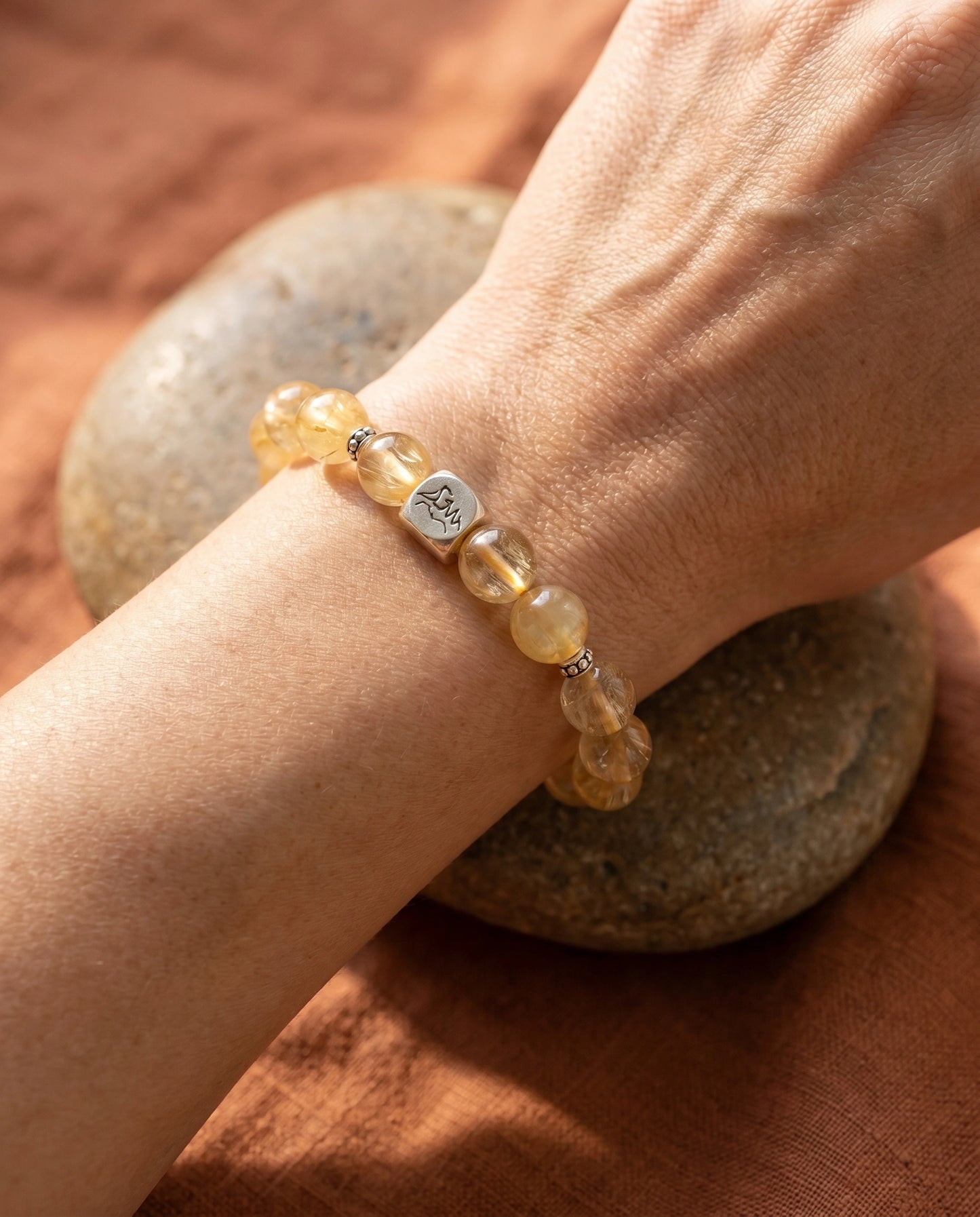 Bastion earth crystal bracelet — golden rutilated quartz — worn on wrist resting on river stone with terracotta linen — Leymen Jewels