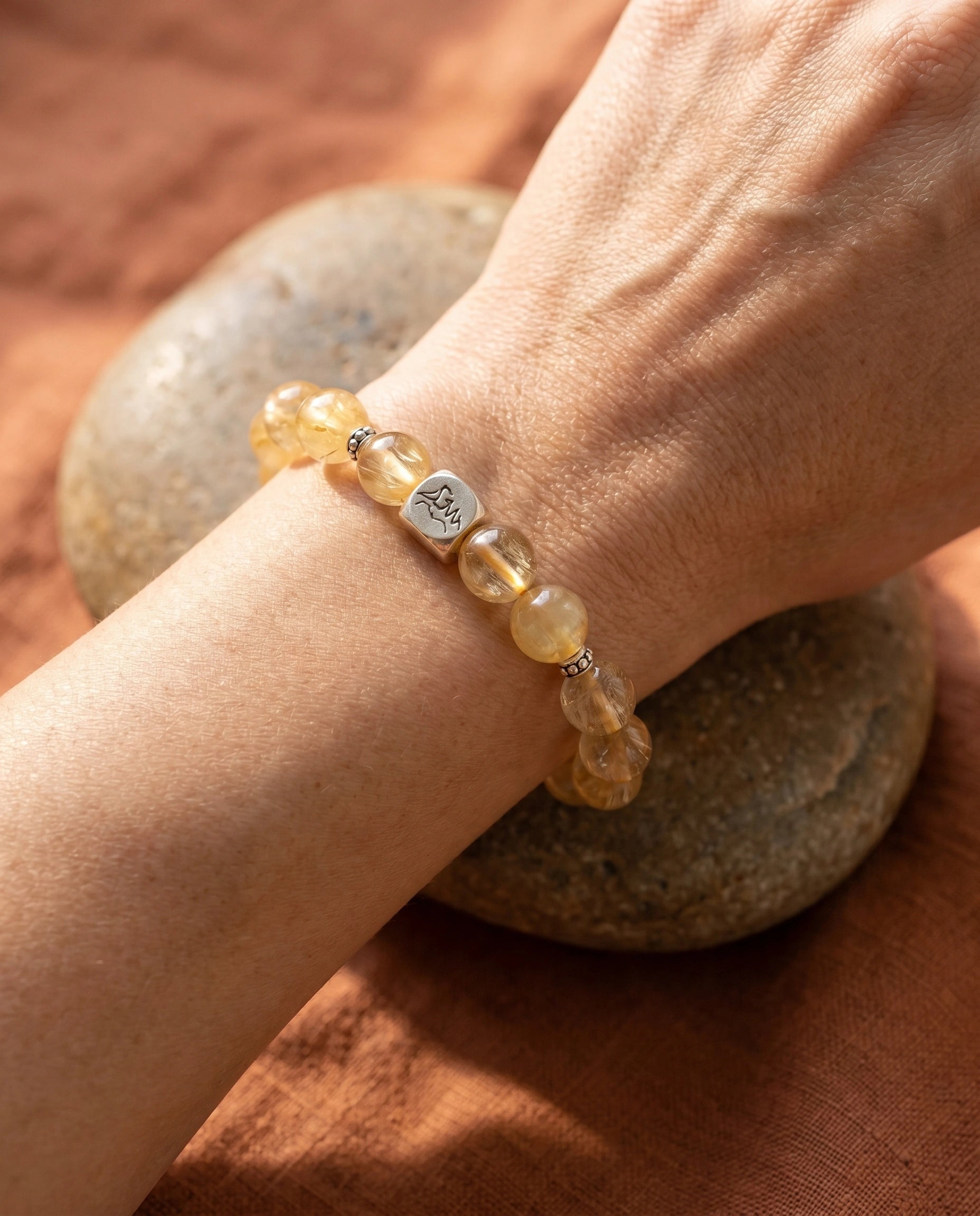 Bastion earth crystal bracelet — golden rutilated quartz — worn on wrist resting on river stone with terracotta linen — Leymen Jewels