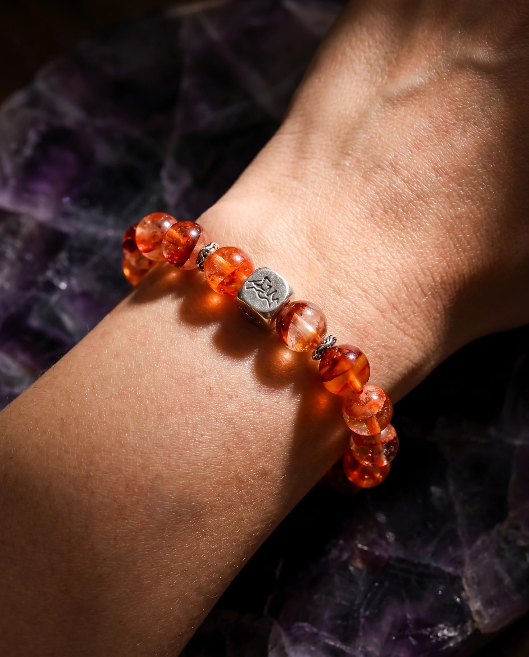 Ember fire crystal bracelet — red phantom quartz — worn on wrist against raw amethyst crystal cluster — Leymen Jewels