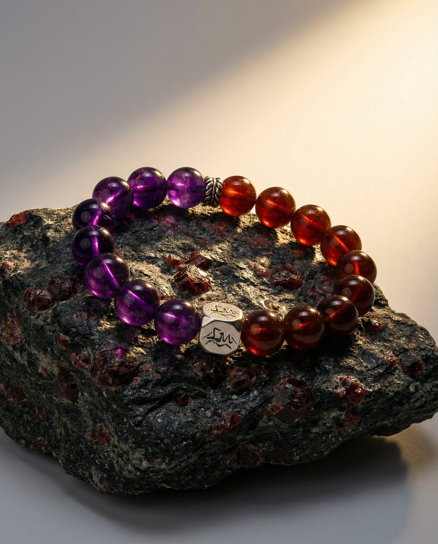 Ignis fire crystal bracelet — amethyst and orange garnet — on dark volcanic rock with warm light — Leymen Jewels