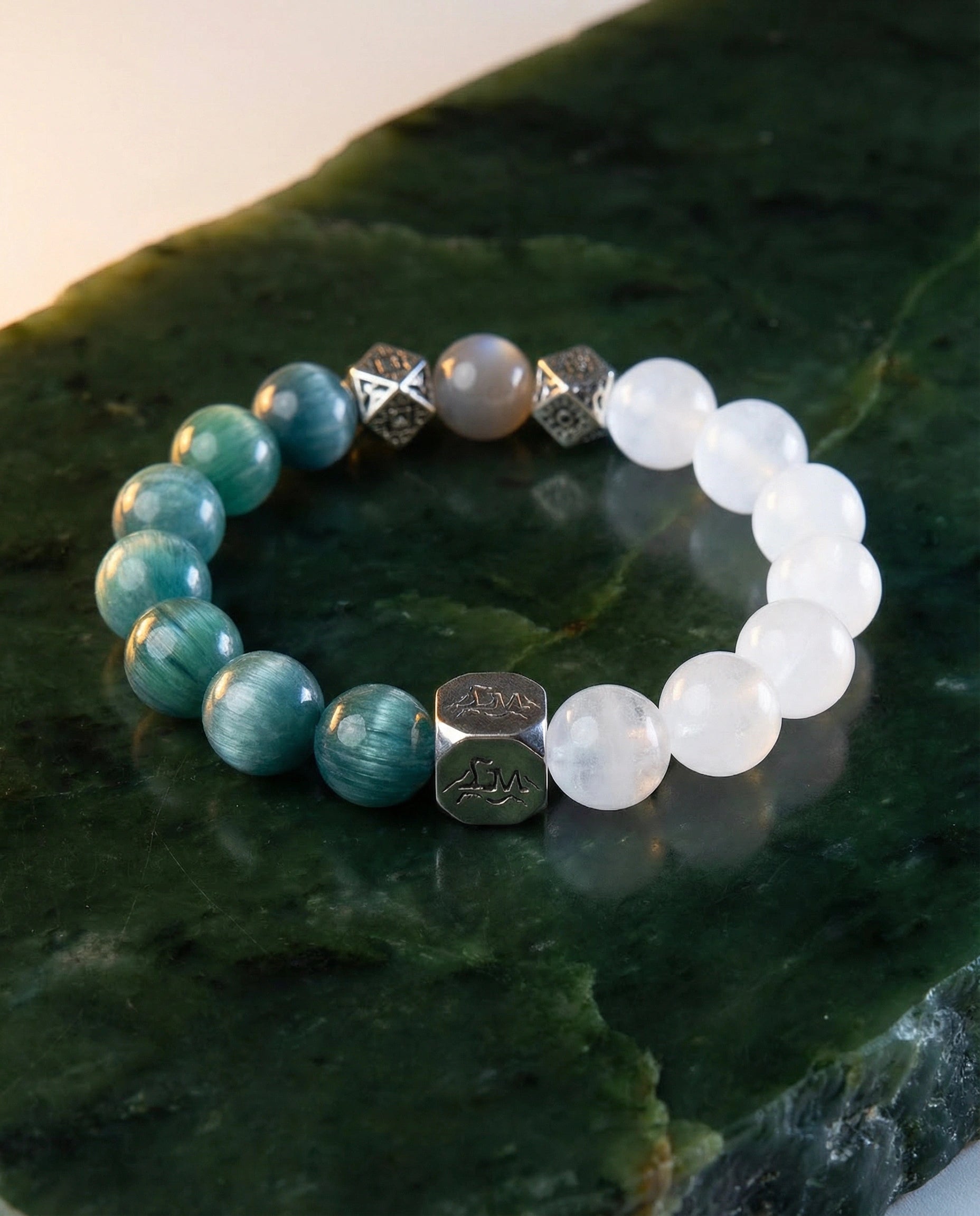 Lumen wood crystal bracelet — teal kyanite and snow quartz — on polished nephrite jade surface with warm light — Leymen Jewels