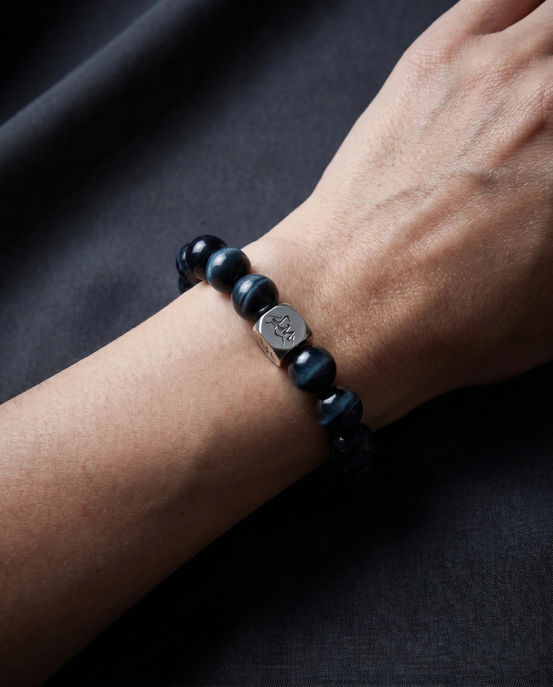 Oracle water crystal bracelet — lapis lazuli and blue tiger's eye — worn on wrist against dark charcoal fabric — Leymen Jewels