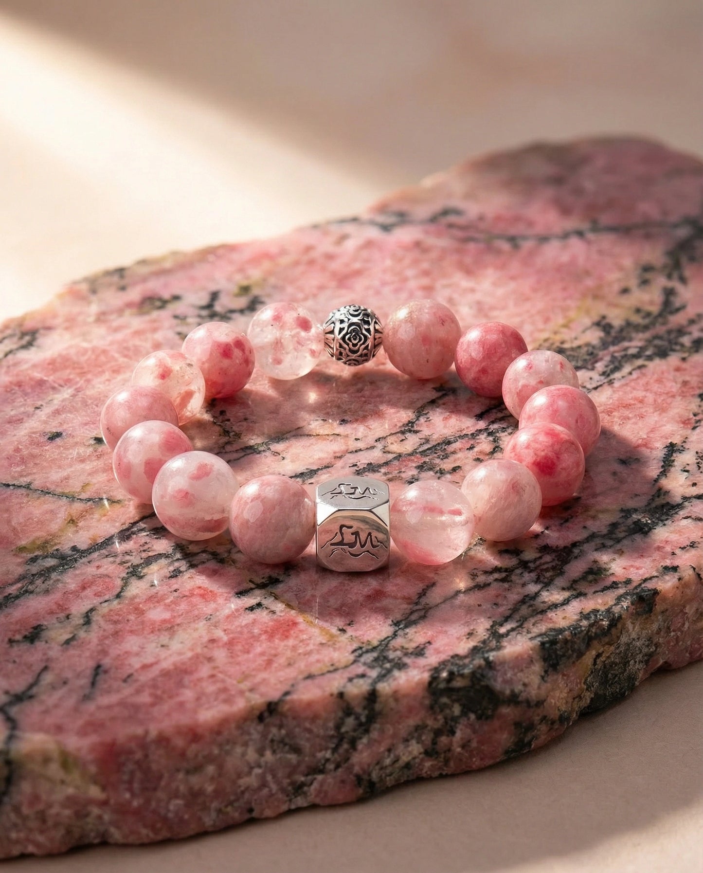 Roseveil fire crystal bracelet — rhodonite — on natural rhodonite mineral slab in warm light — Leymen Jewels