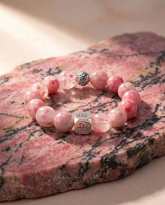 Roseveil fire crystal bracelet — rhodonite — on natural rhodonite mineral slab in warm light — Leymen Jewels