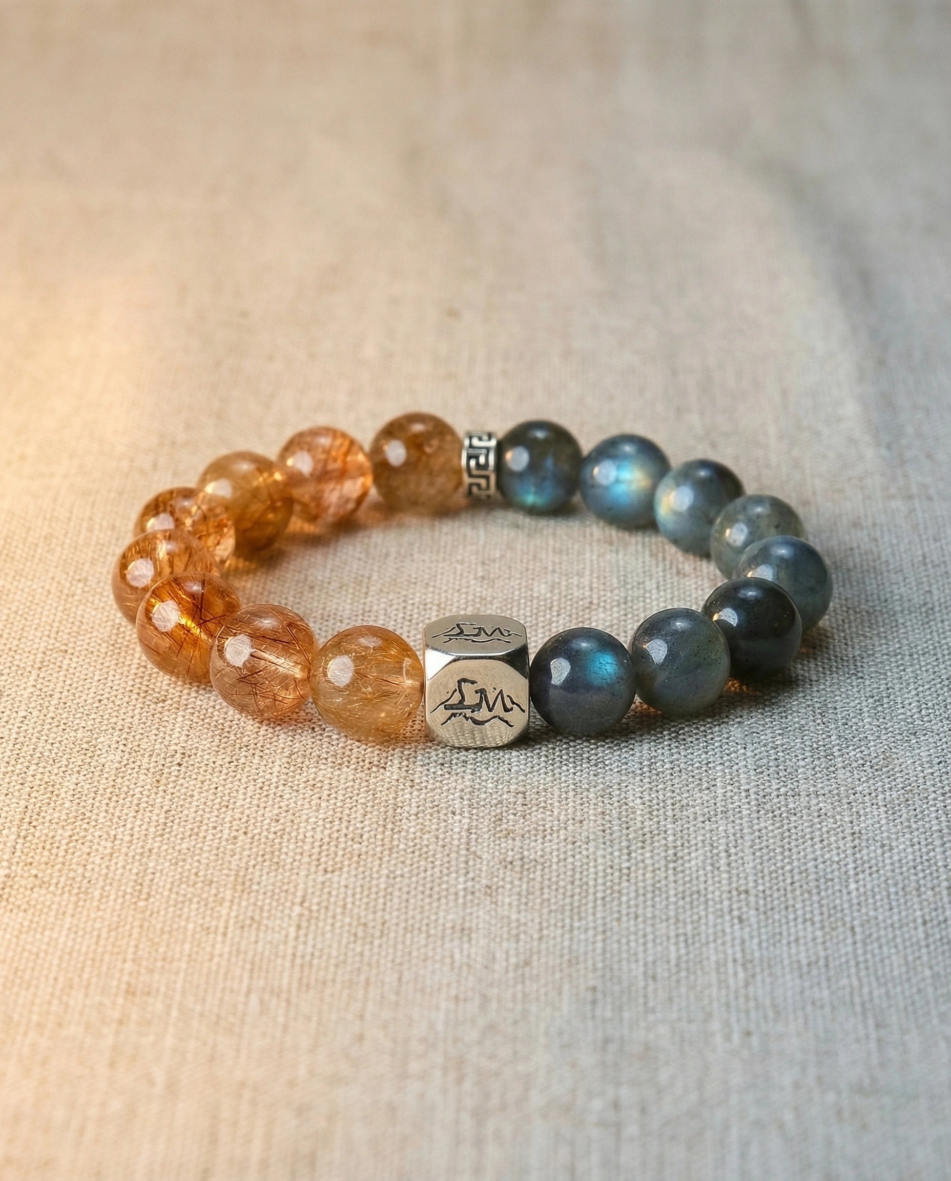 Solace metal crystal bracelet — copper rutilated quartz and grey moonstone — on natural linen surface with warm light — Leymen Jewels
