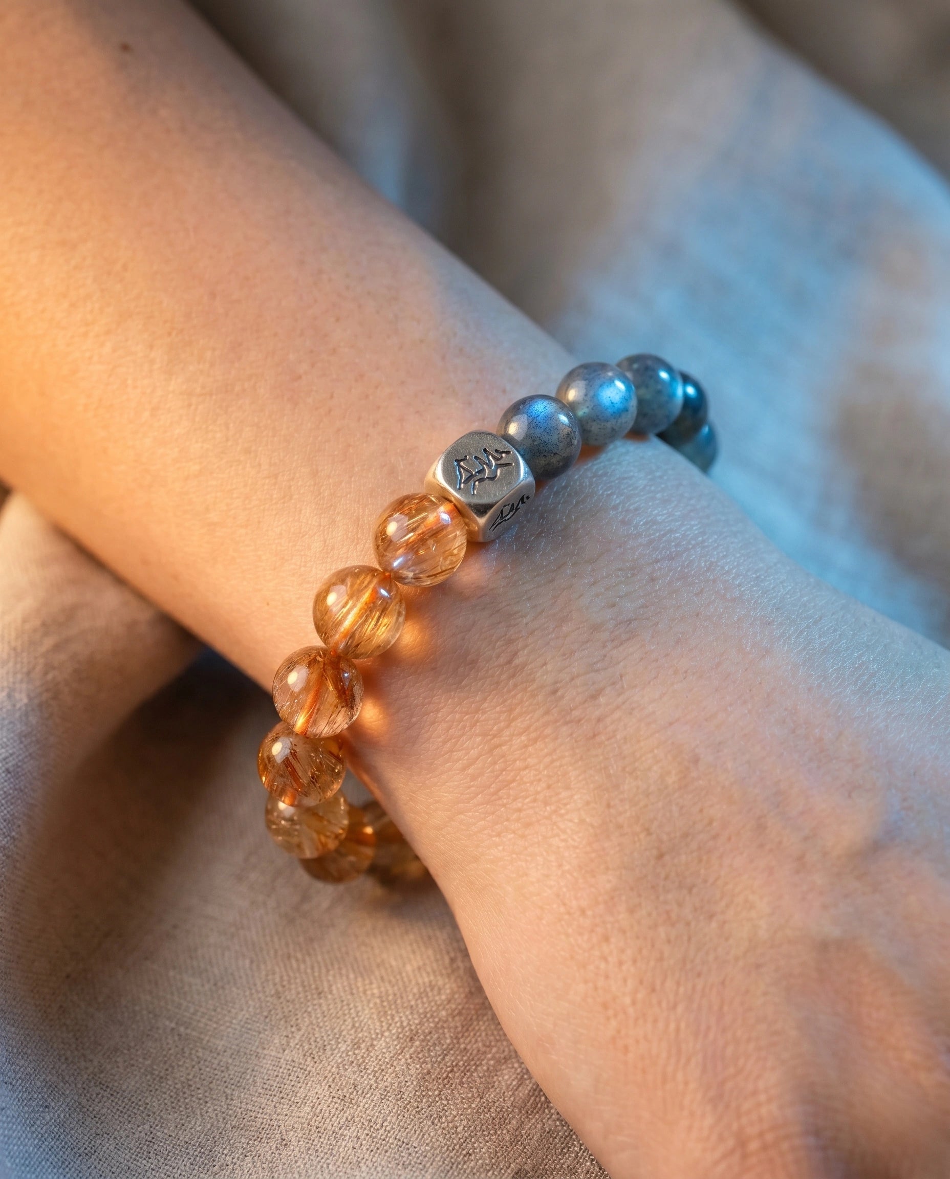 Solace metal crystal bracelet — copper rutilated quartz and grey moonstone — worn on wrist on warm linen — Leymen Jewels